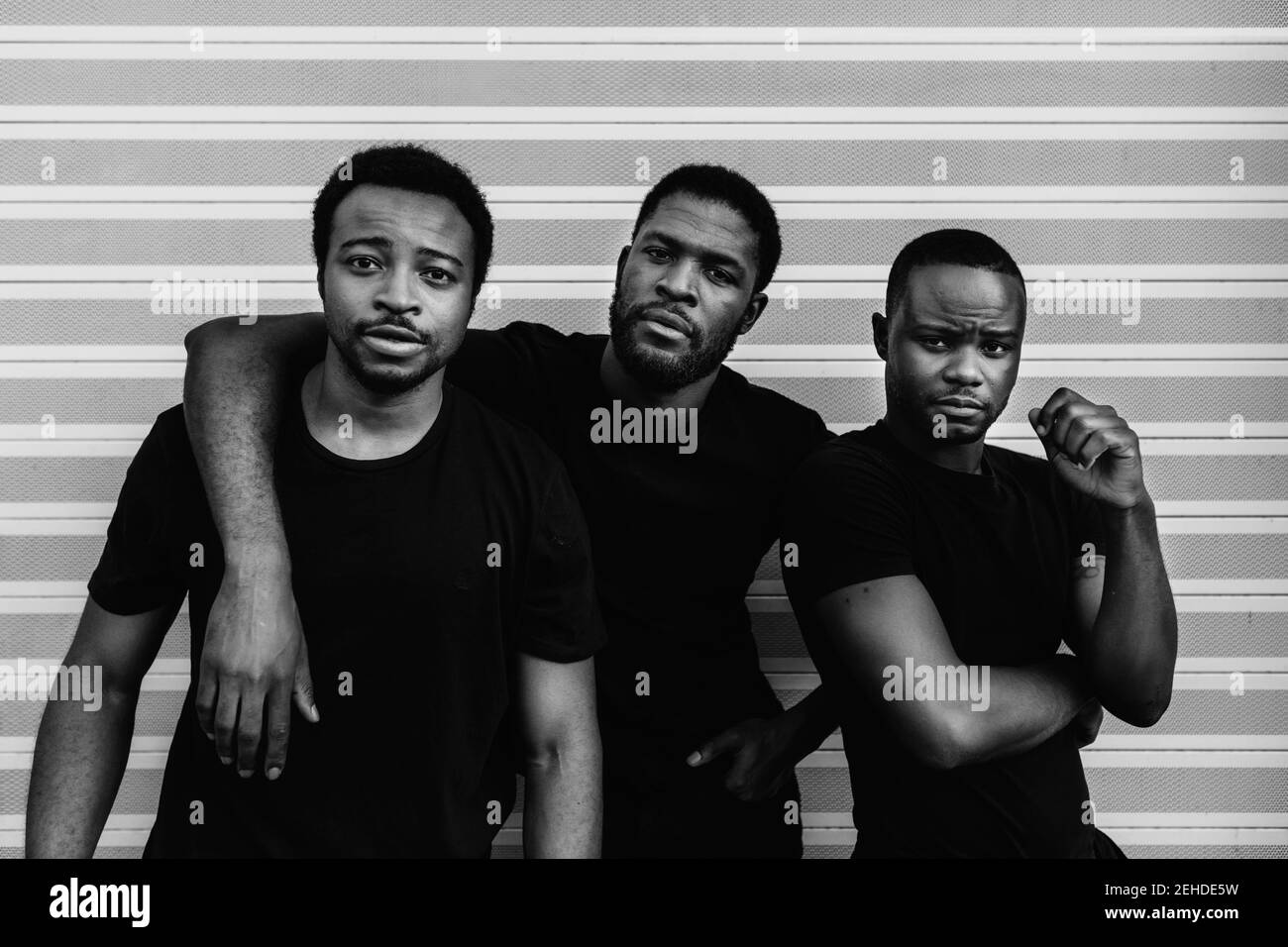 Seriöse afroamerikanische Freunde in schwarzen T-Shirts stehen nah Beim Betrachen der Kamera auf hellem Hintergrund Stockfoto