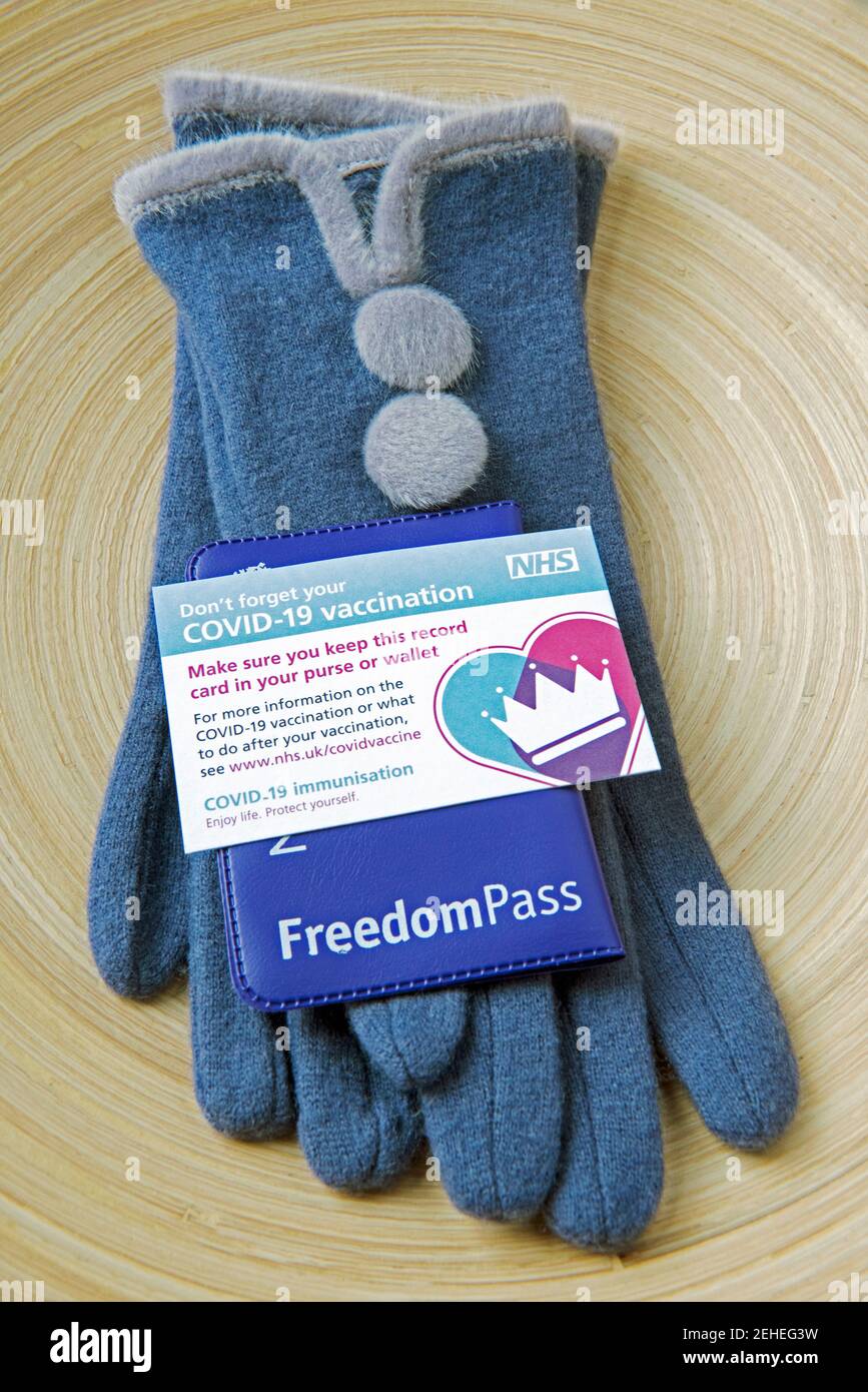 Covid-19 Impfkarte oder Impfkarte mit Freedom Pass auf Damen blauen Handschuhen. Reisefreiheit Konzept für ältere Menschen nach ihrem Covid Jab Stockfoto