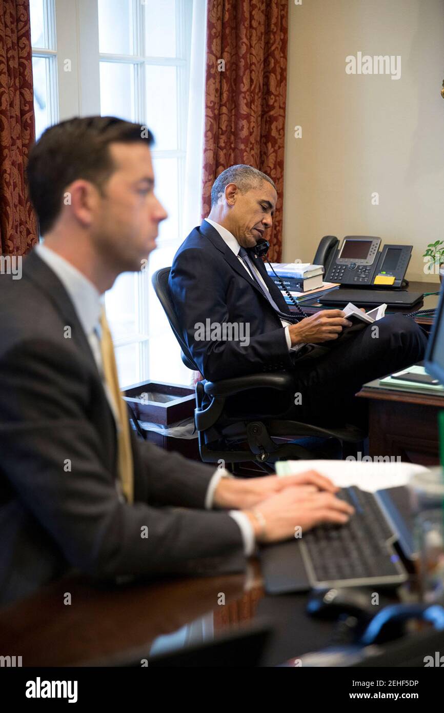 Präsident Barack Obama spricht am Telefon mit Haus demokratische Führer Nancy Pelosi, D -Calif., sitzend im äußeren Oval Office, 26. März 2015. Brian Mosteller, Director of Operations Oval Office, arbeitet an seinem Schreibtisch. Stockfoto