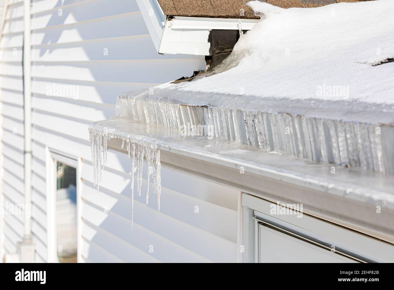 Dachrinne voller Eis und Eiszapfen nach dem Wintersturm. Konzept von Dachschäden, Hauswartung und Reparatur. Stockfoto