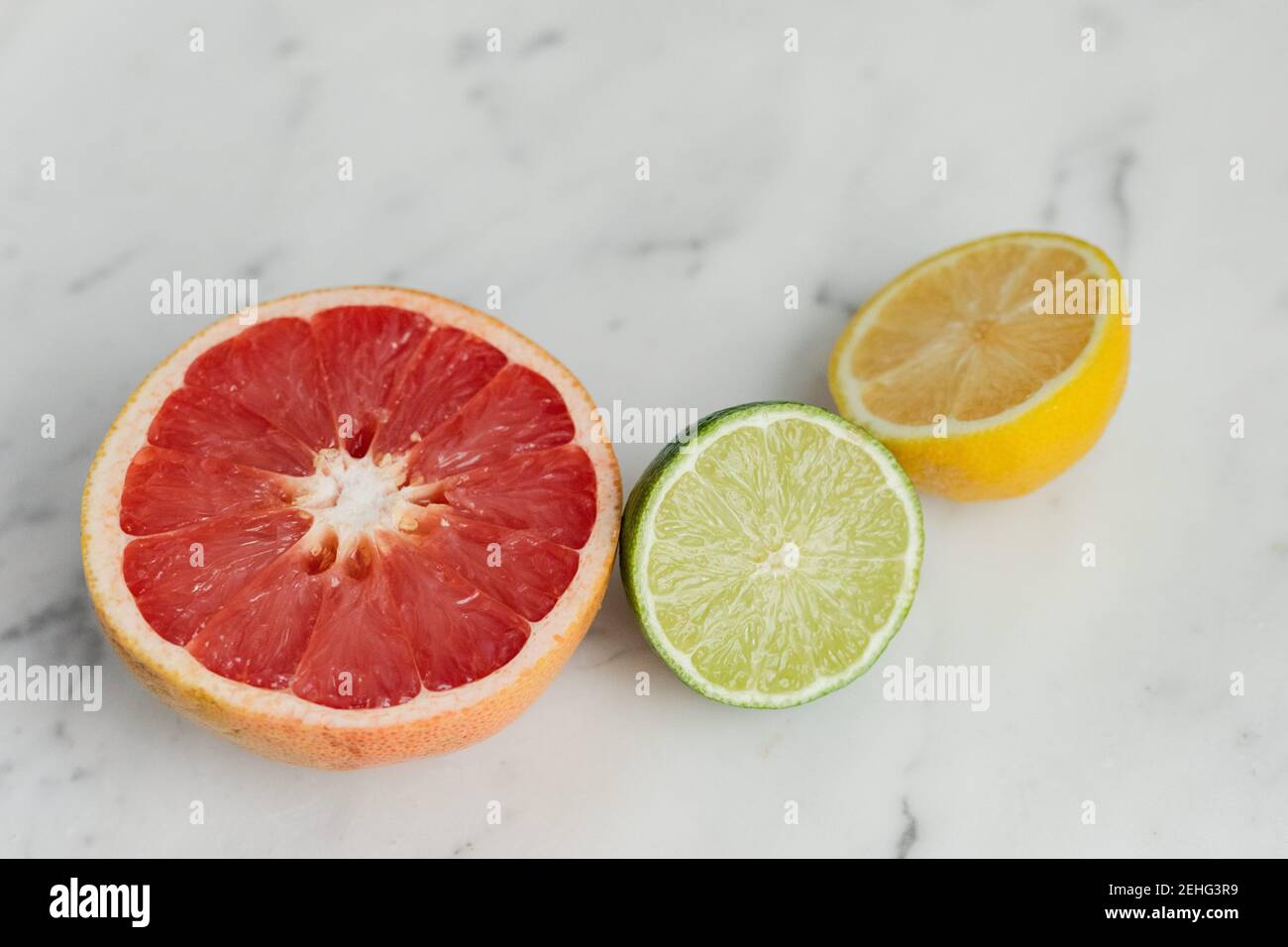 Frische Zitrusfrüchte, Grapefruit, Zitrone und Limette, geschnitten auf einem Marmorhintergrund Stockfoto