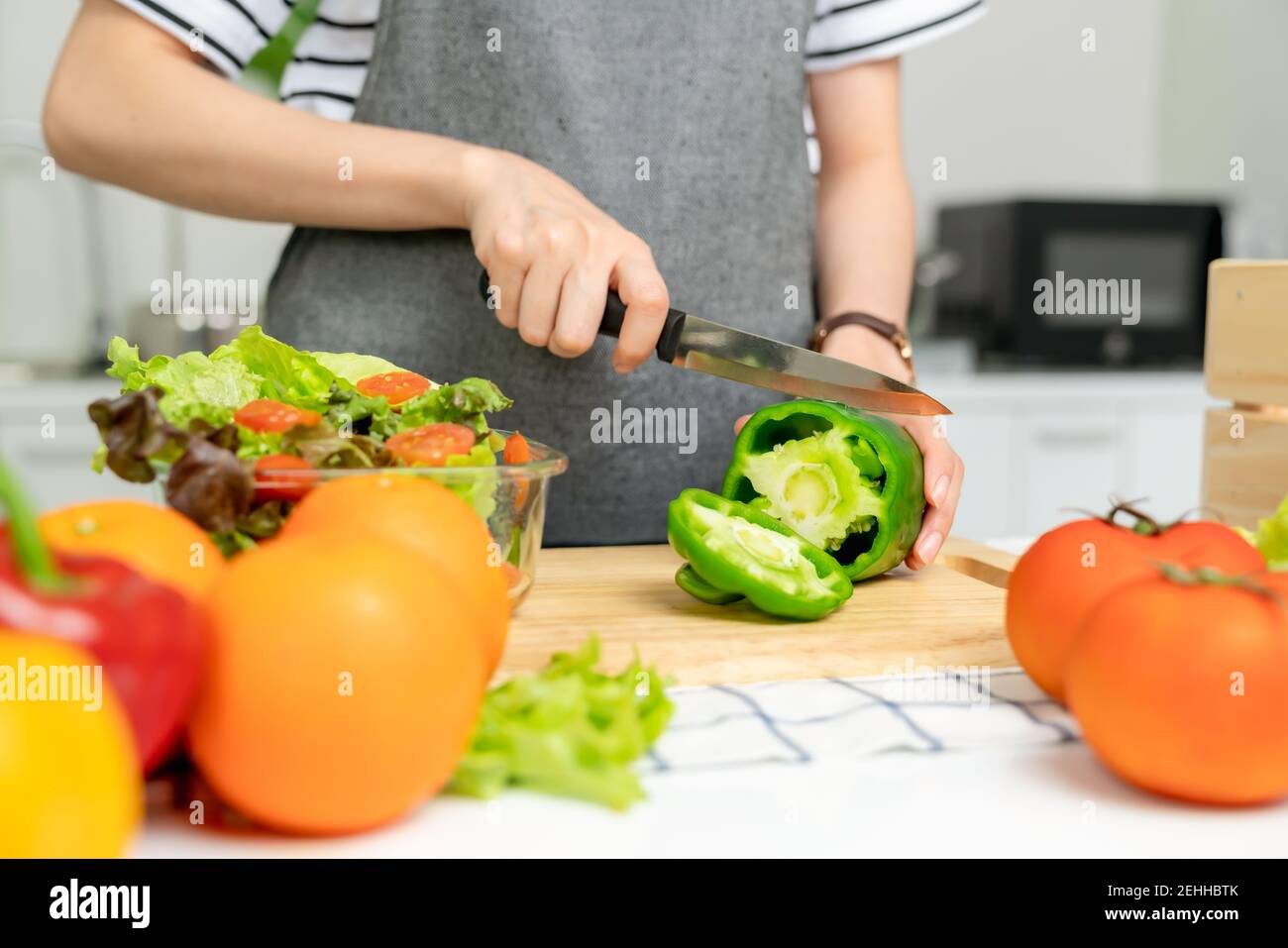 Nahaufnahme der Frau Hände Verwenden Sie ein Messer, um die Paprika und verschiedene grüne Blattgemüse auf dem Tisch zu Hause schneiden. Stockfoto