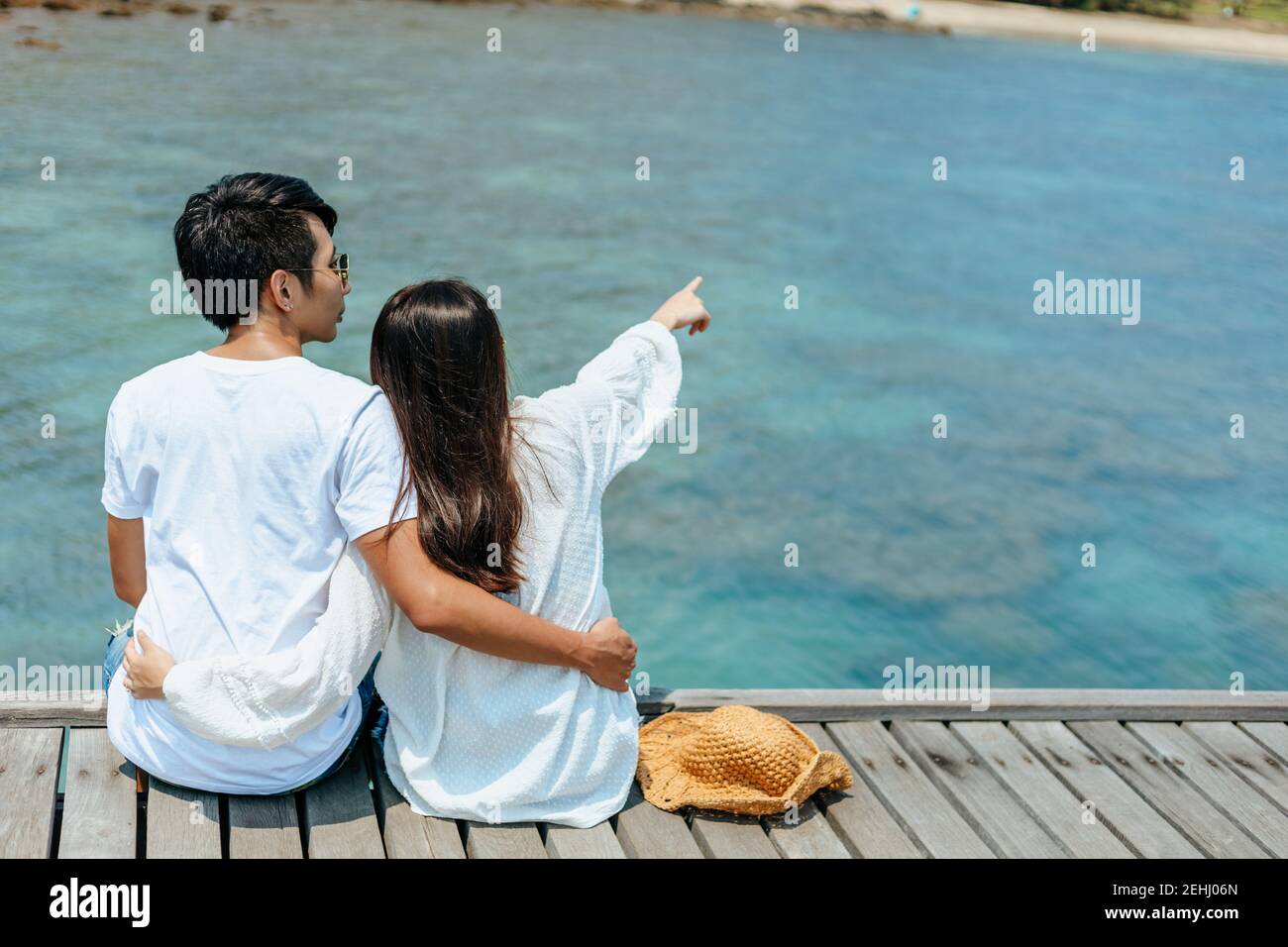 Flitterwochen romantoc Paar umarmt und sitzt auf Holzbrücke und genießt ihren tropischen Urlaub. Liebeskonzept. Stockfoto