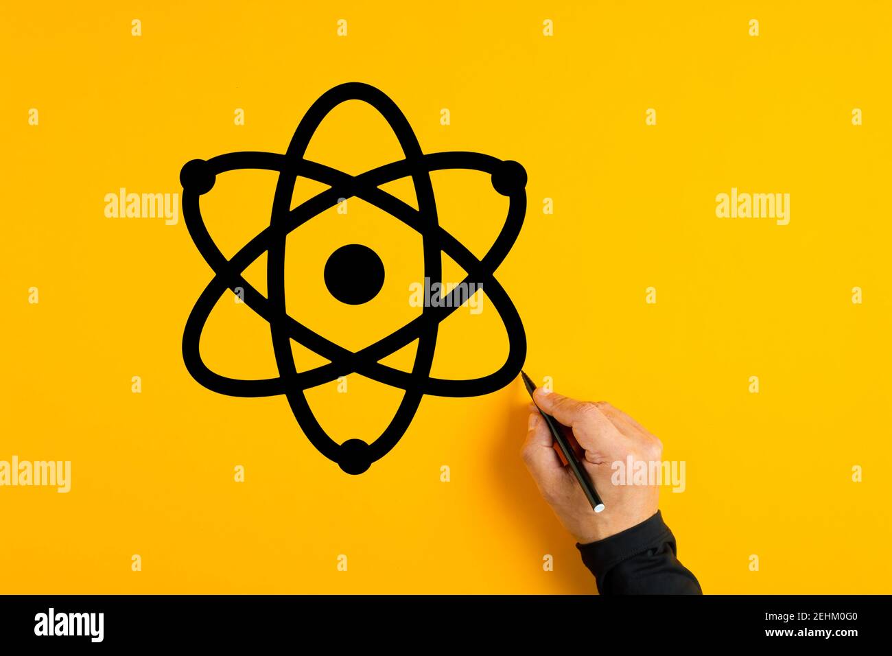 Männliche Hand zeichnet ein Atom-Symbol auf gelbem Hintergrund. Wissenschaft und Technik Konzept. Stockfoto