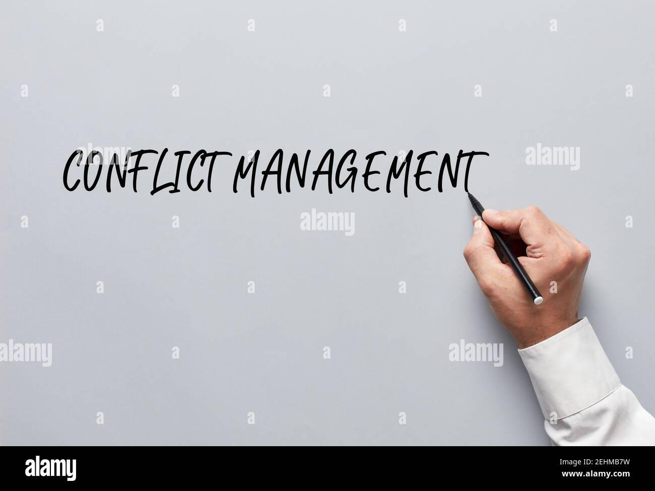 Männliche Hand schreiben Konfliktmanagement auf grauem Hintergrund. Konfliktlösung im Business Workplace Konzept. Stockfoto