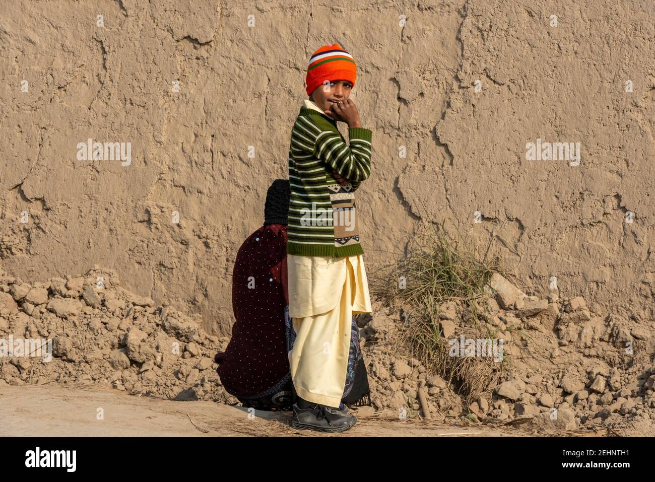 Dorfjunge, der vor einer braunen Mauer steht, Punjab, Pakistan Stockfoto