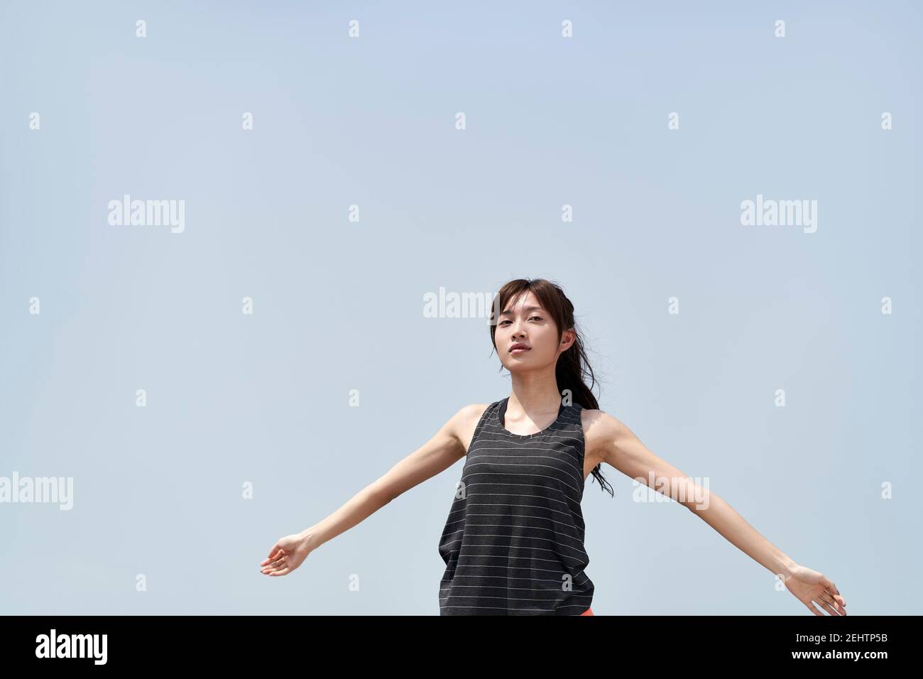 Junge asiatische Frau in Sportbekleidung im Freien gegen blauen Himmel stehen Mit offenen Armen Stockfoto