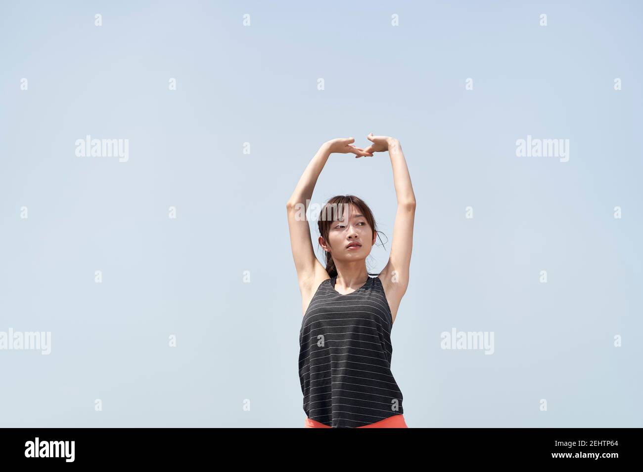 Junge asiatische Frau in Sportkleidung Stretching Arme im Freien gegen blau Himmel Stockfoto
