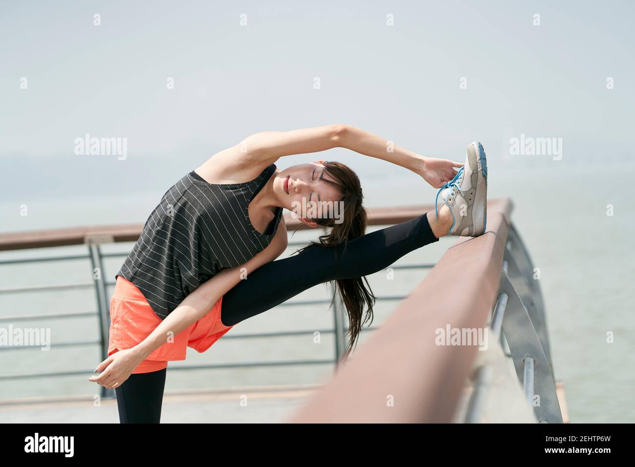Junge asiatische Frau in Sportswear Stretching Körper im Freien in Meer parken Stockfoto