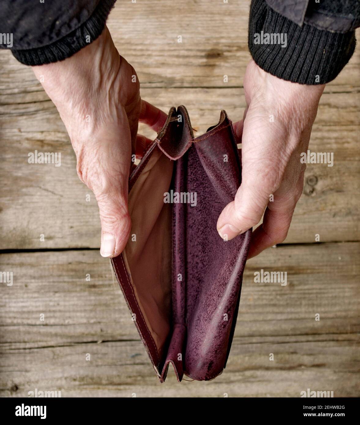 Eine ältere Frau hält eine leere Handtasche oder Brieftasche auf einem hölzernen Vintage-Tisch. Das Konzept der Armut im Ruhestand. Globale extreme Armut. Kein Geld hilft mir. Stockfoto