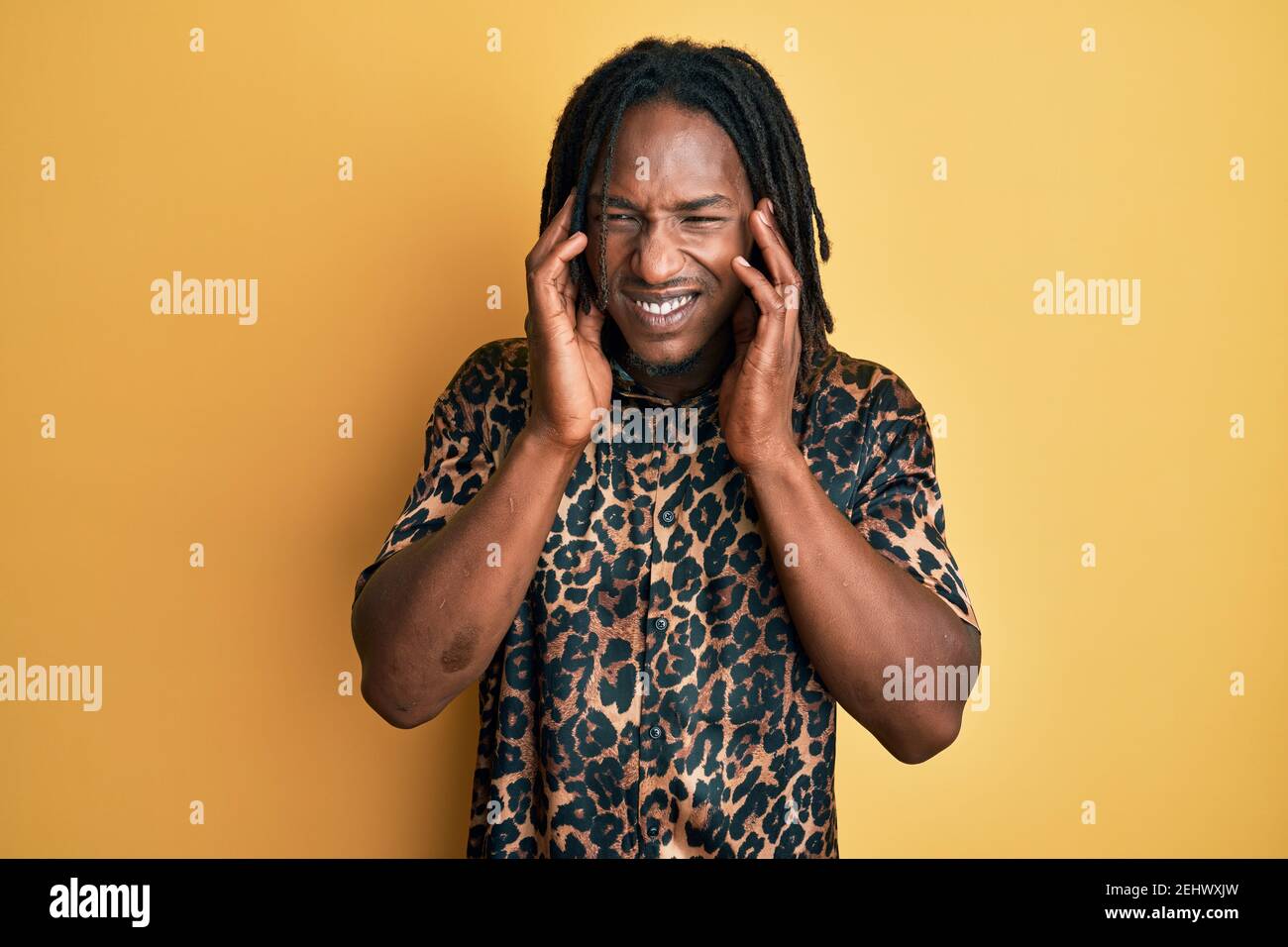 Afroamerikanischer Mann mit Zöpfen trägt Leoparden Tier drucken Hemd bedeckt Ohren mit Fingern mit verärgerten Ausdruck für den Lärm der lauten Musik. De Stockfoto