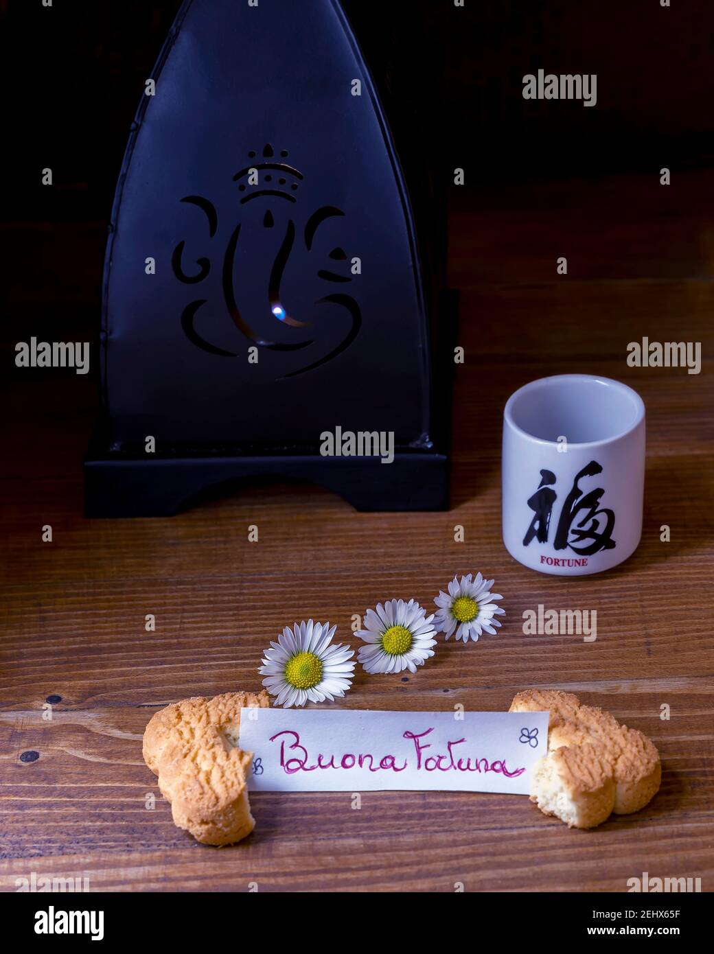 Ein Keks in der Hälfte mit dem italienischen Satz, die gespalten Bedeutet Glück und eine Tasse mit dem japanischen Wort Glück auf einem dunklen Hintergrund Stockfoto