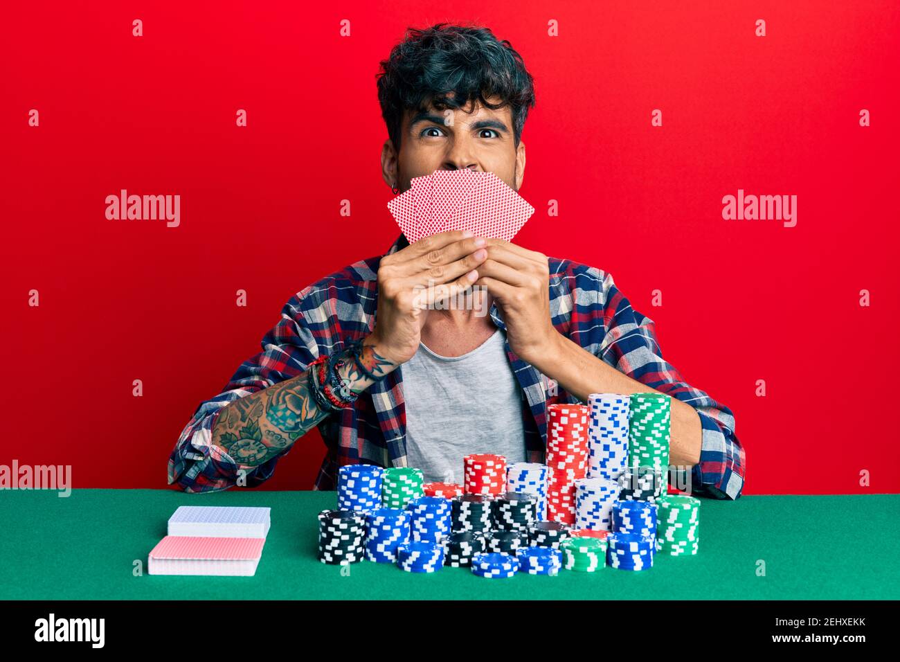 Junge hispanic Mann spielen Glücksspiel Poker Abdeckung Gesicht mit Karten ragen Zunge aus glücklich mit lustigen Ausdruck. Stockfoto