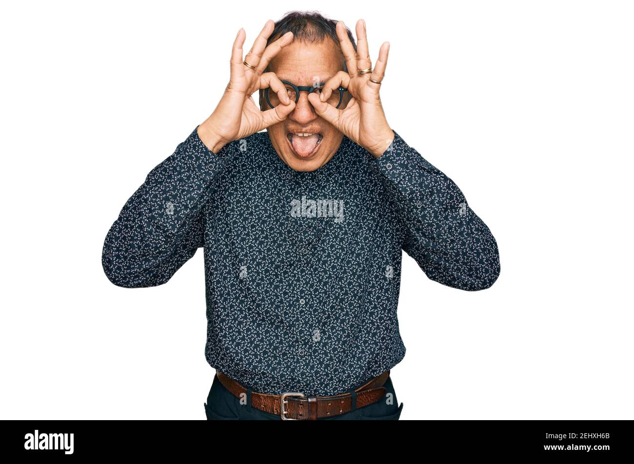 Mittelalter indischer Mann trägt lässige Kleidung und Brille tun ok Geste wie Fernglas aufragende Zunge aus, Augen durch die Finger schauen. Verrückte exp Stockfoto