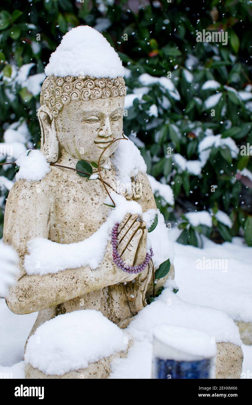 Buddha Steinstatue unter dem Schnee in der Wintersaison in einem Garten. Stockfoto