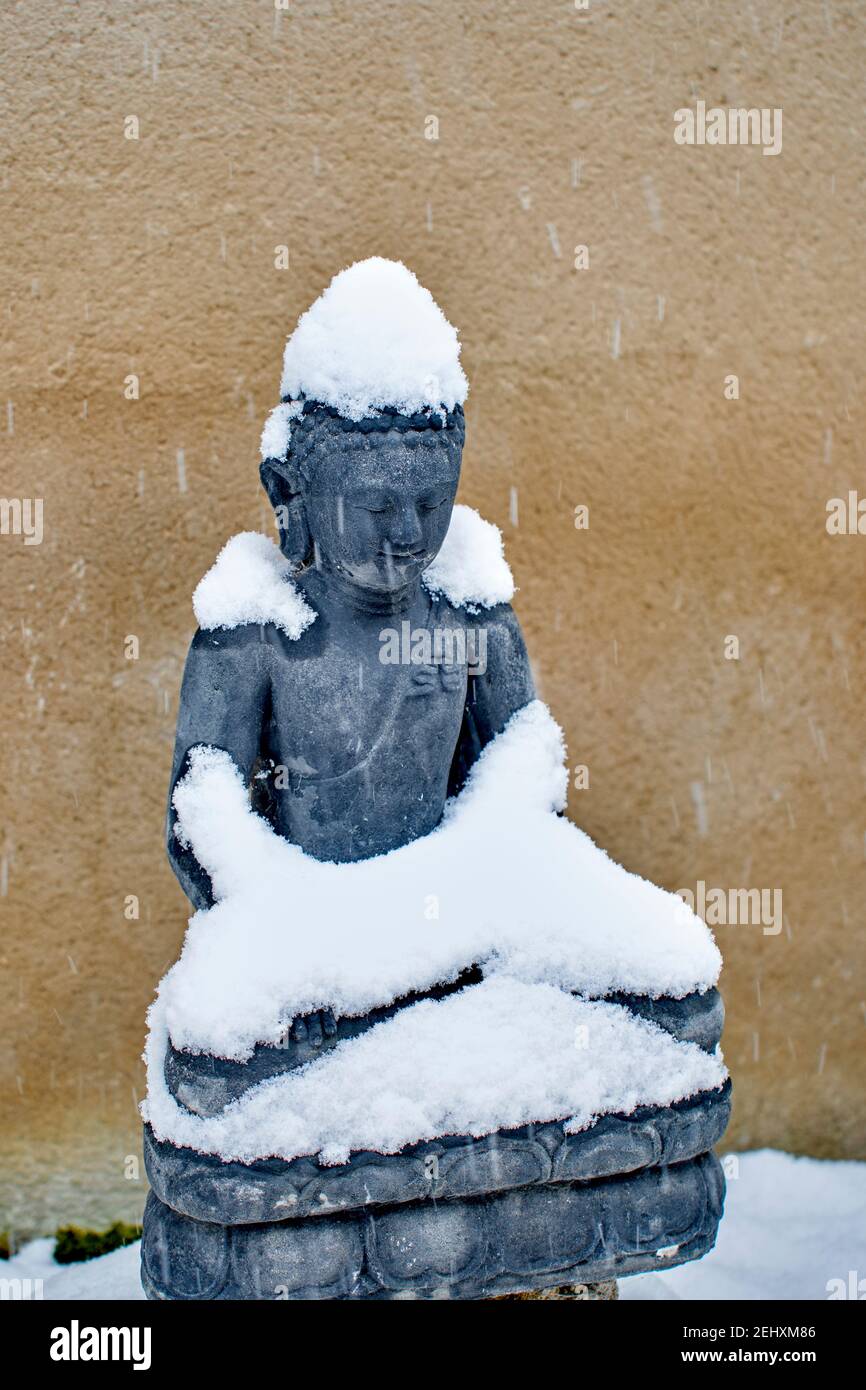 Buddha Steinstatue unter dem Schnee in der Wintersaison in einem Garten. Stockfoto