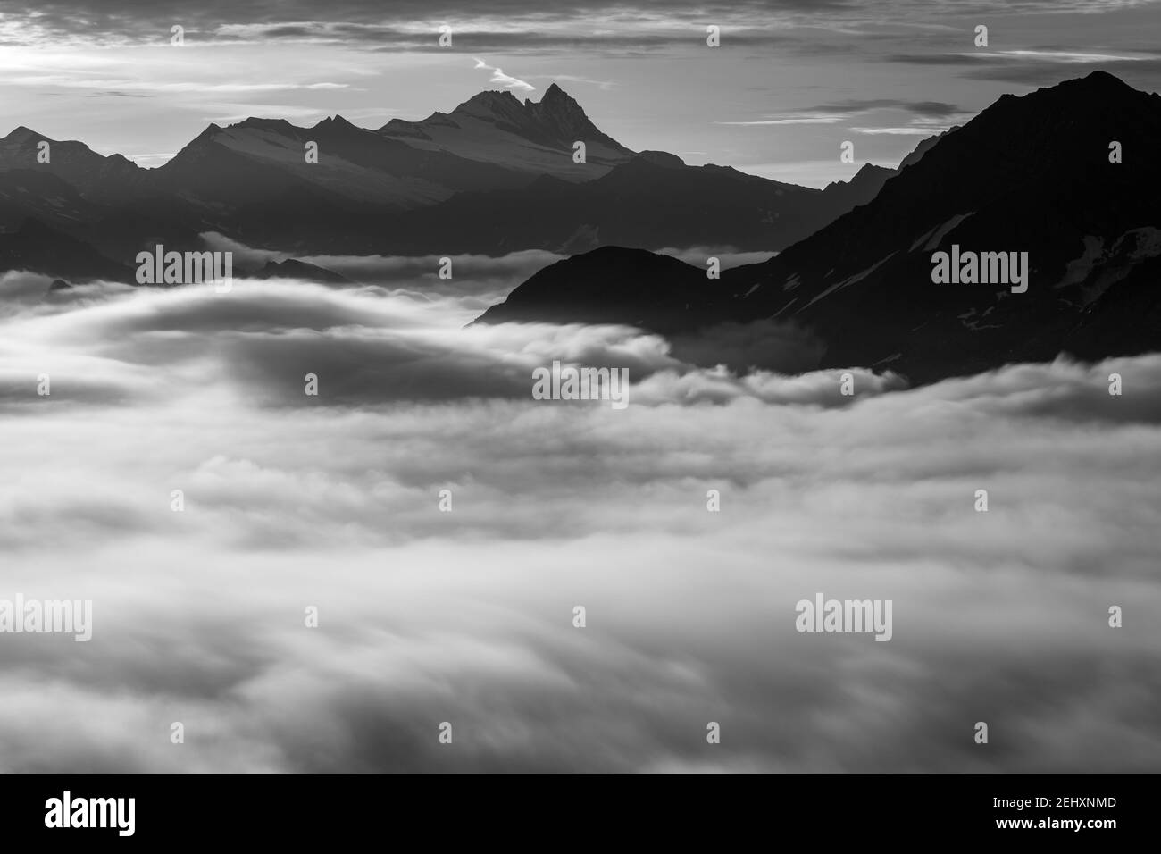 Blick auf die Westseite der Glockner-Gruppe. Großglockner Berggipfel. Sich bewegende Wolken. Österreichische Alpen. Europa. Schwarz-weiße Landschaft. Stockfoto
