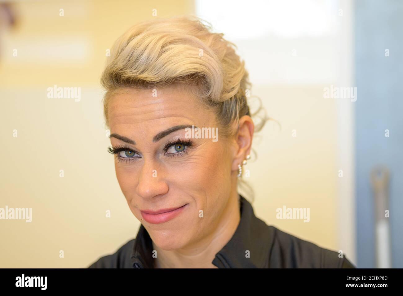 Lächelnde blonde Frau mittleren Alters trägt falsche Wimpern und Make-up posiert Blick auf die Kamera in einer Nahaufnahme Kopf aufgenommen in Türen Stockfoto