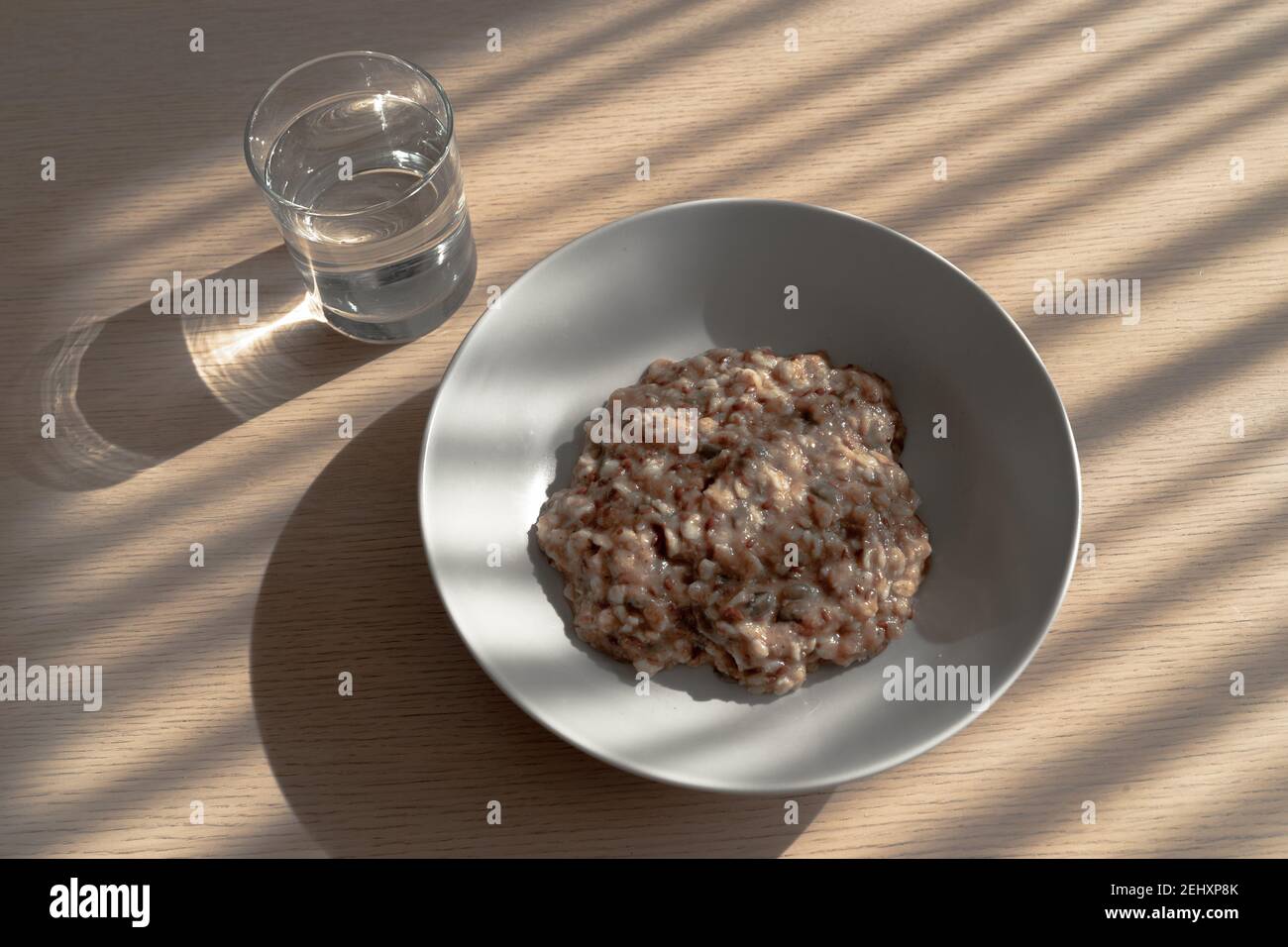 Gesundes Frühstück auf Holztisch: Ein Glas Wasser und ein Teller warmen Haferbrei Haferbrei mit Leinsamen, Kürbiskernen. Stockfoto