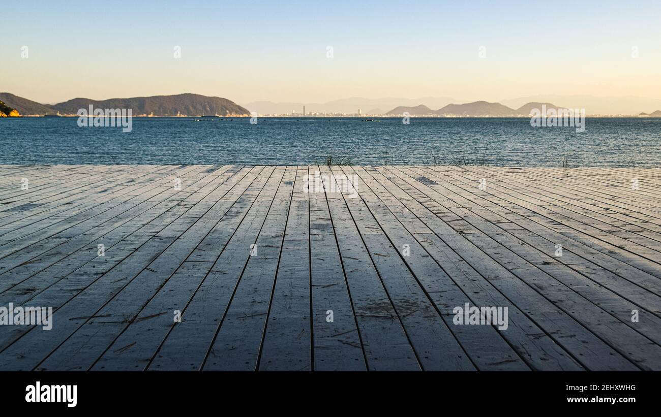 Blick auf das Meer von der Holzterrasse mit zwei Pinien am Ufer der Naoshima Insel, Japan, während der Sonnenuntergang mit der Great Seto Brücke trübe Stockfoto