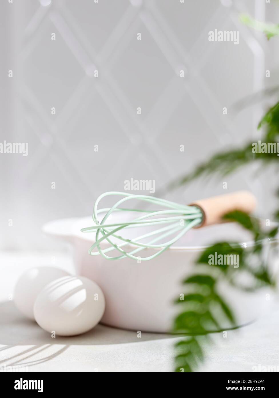 Eierbesen, mit einem Holzgriff, Eiern und einer weißen Schüssel auf weißem Hintergrund reinigen. Selektiver Fokus Stockfoto