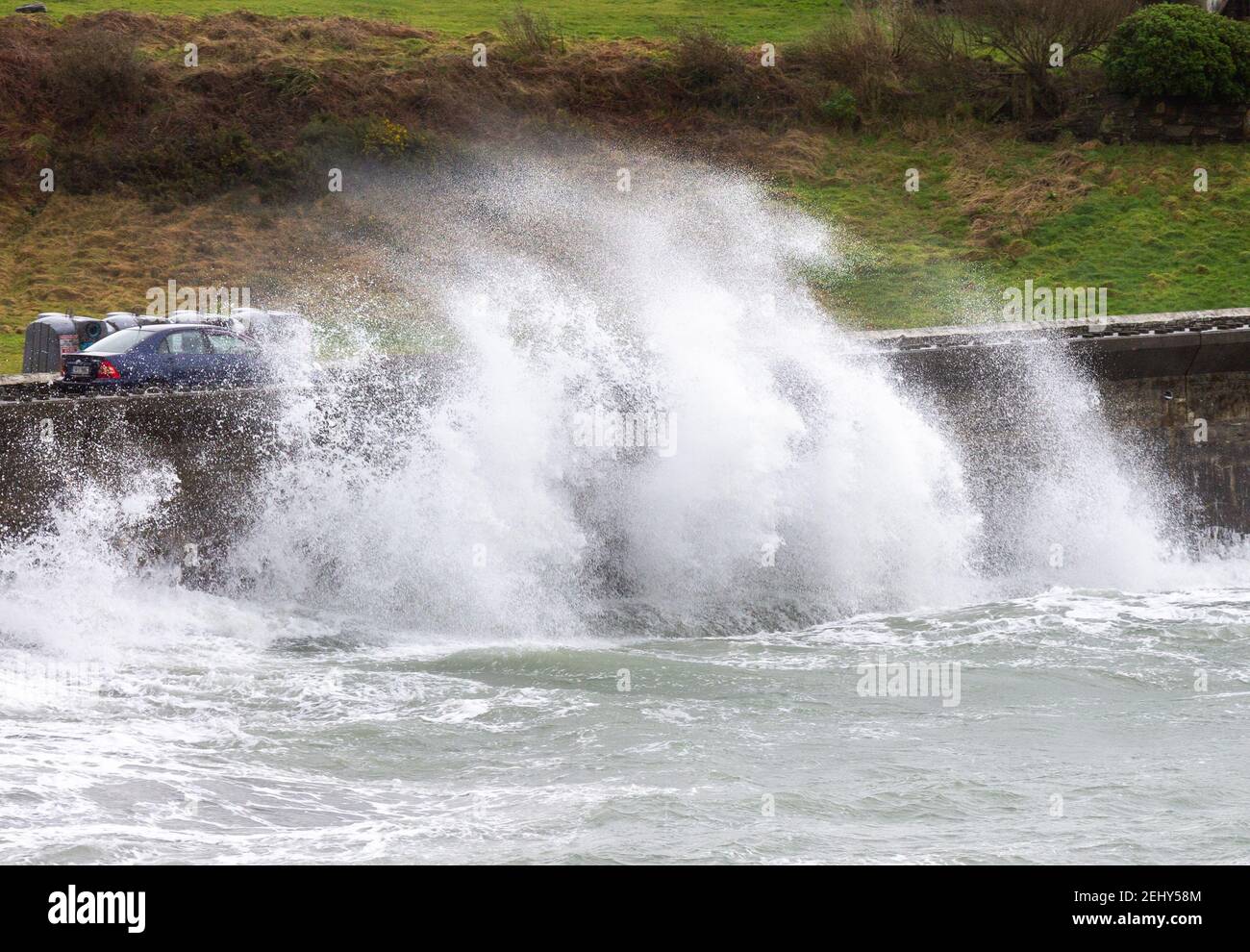 Winter Sturmwellen brechen über der Meereswand und bedecken das vorbeifahrende Auto. Stockfoto