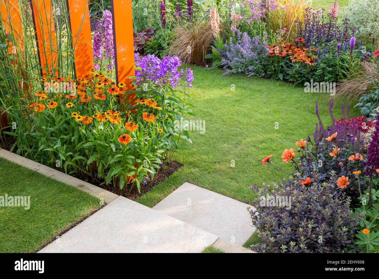 Ein kleiner englischer Garten - Steintreppe führt zu einem Rasengras mit Blumenbeeten gefüllt mit Blumen Pflanzen einschließlich Helenium - Dahlien England GB UK Stockfoto