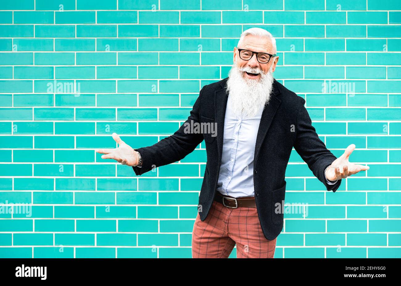 Fröhlicher Hipster Mann auf Willkommens-Stimmung posiert gegen türkisfarbene Wand Hintergrund - trendige alte Person tragen lässige Mode Kleidung - Glückliches älteres Leben Stockfoto