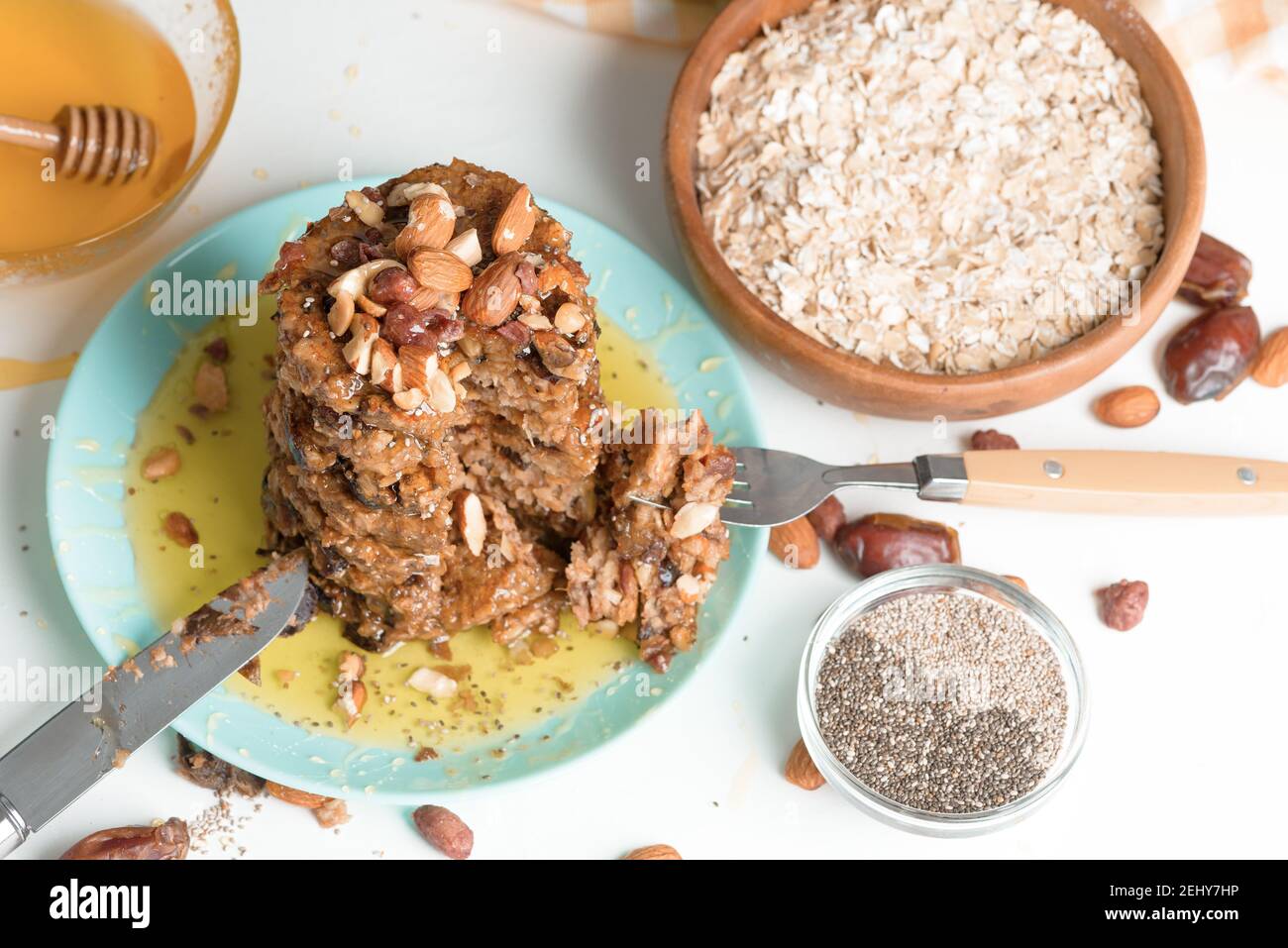 Hausgemachte Haferflocken Banane Pfannkuchen mit Chiasamen, Mandeln, Pflaumen und Datteln, beträufelt mit Honig und zerkleinerten Nüssen auf einem dunklen Hintergrund. Diät-Frühstück Stockfoto