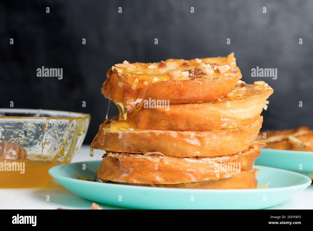 Hausgemachter French Toast gebraten mit Honig und Nüssen auf einem blauen Teller auf einem dunklen Hintergrund. Eingeweicht in Milch-Ei-Mischung. Gesundes Frühstück. Nahaufnahme. Stockfoto