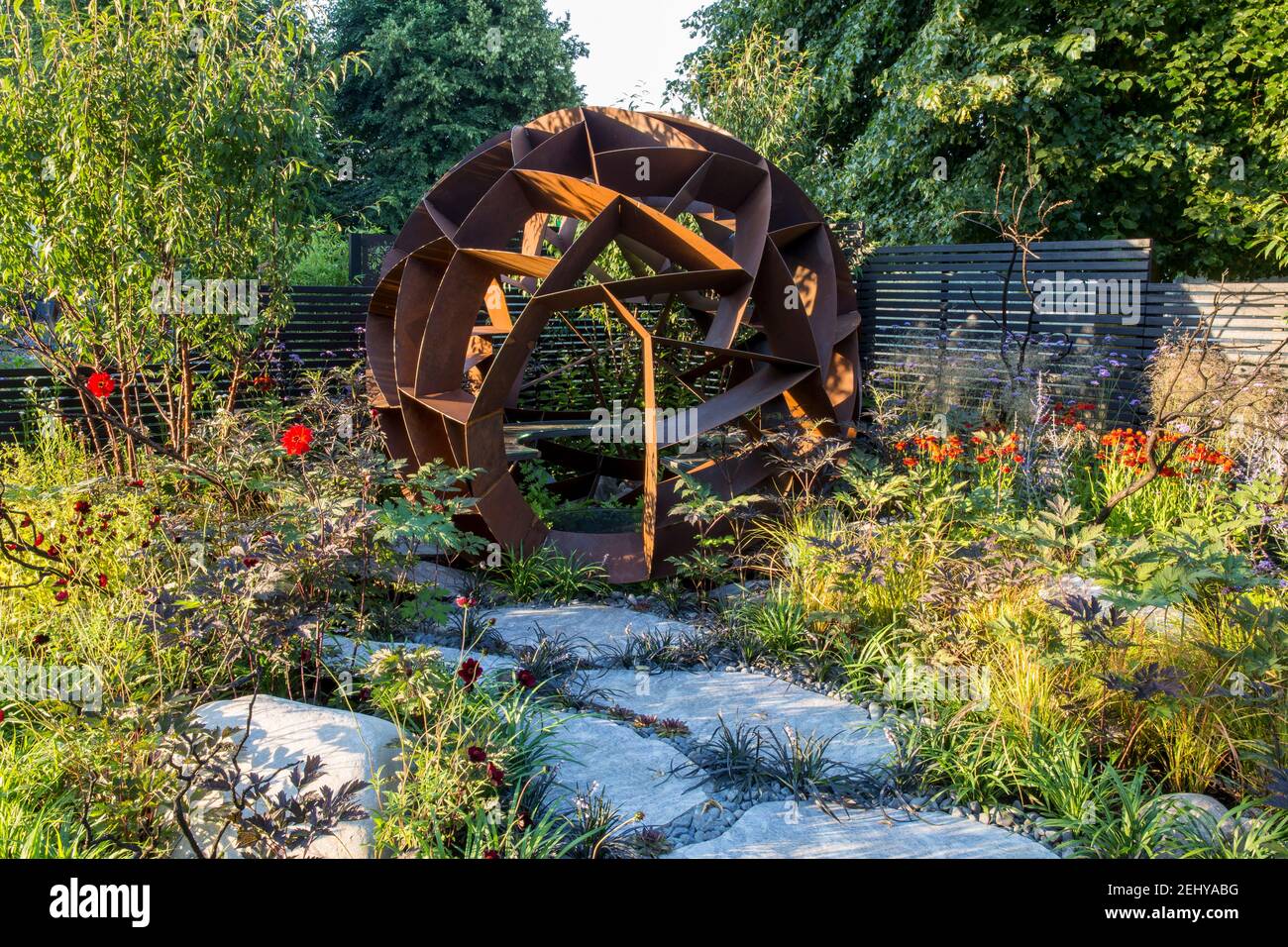 Zeitgenössischer Garten mit großen Caledonischen Steinpflasterplatten Pfad aus kortenförmigem Stahlbau Sitzbereich mit Sommerblumenbeeten grenzt an England GB Großbritannien Stockfoto