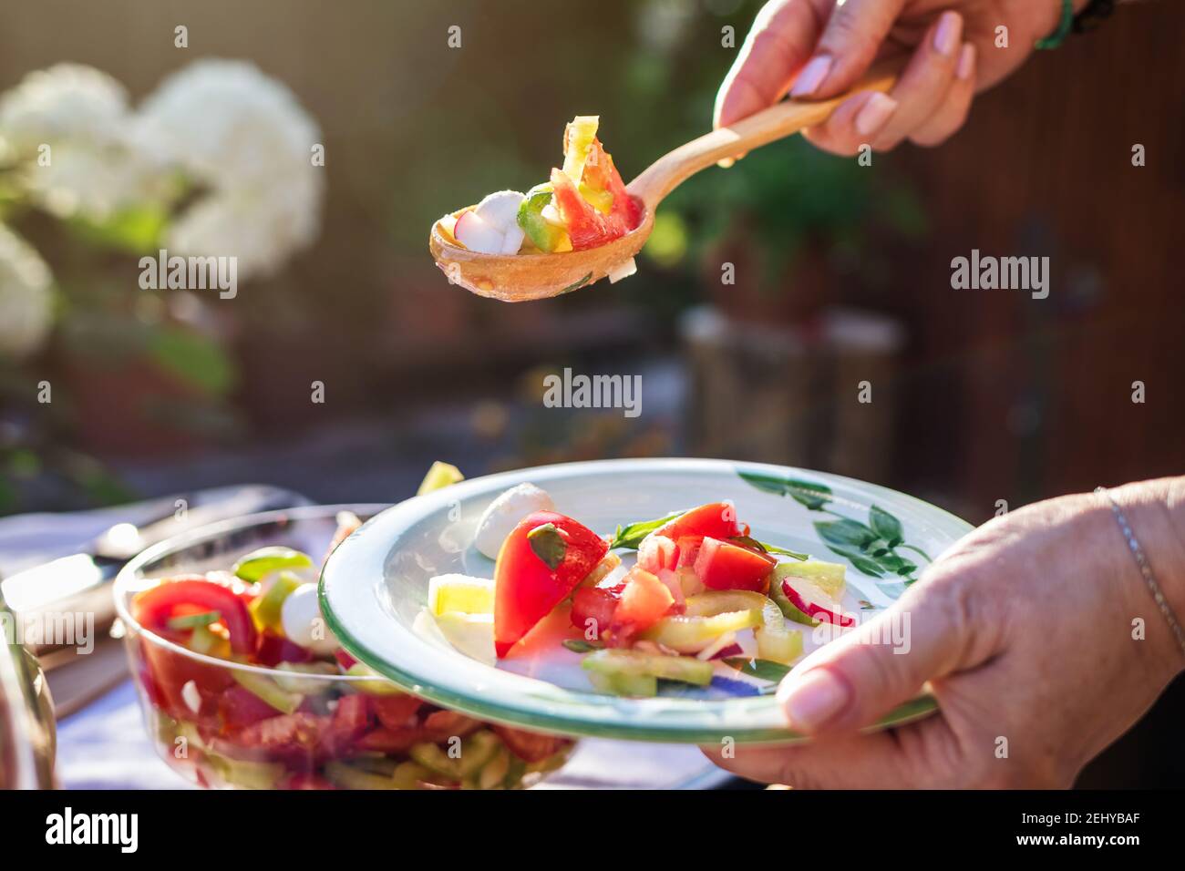 Frau serviert Gemüsesalat mit Holzlöffel auf dem Teller. Genießen Sie gesunde vegetarische Speisen im Freien. Stockfoto