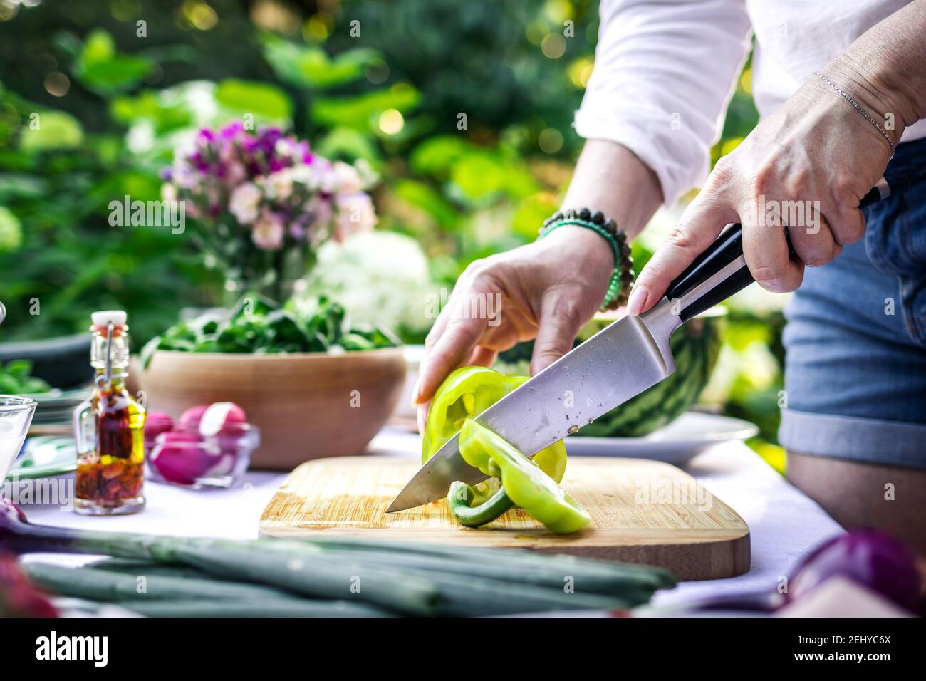 Schneiden von grünen Paprika mit Küchenmesser. Frau kocht Gemüsesalat auf dem Tisch im Freien. Vorbereitung Essen für Garten Party Stockfoto