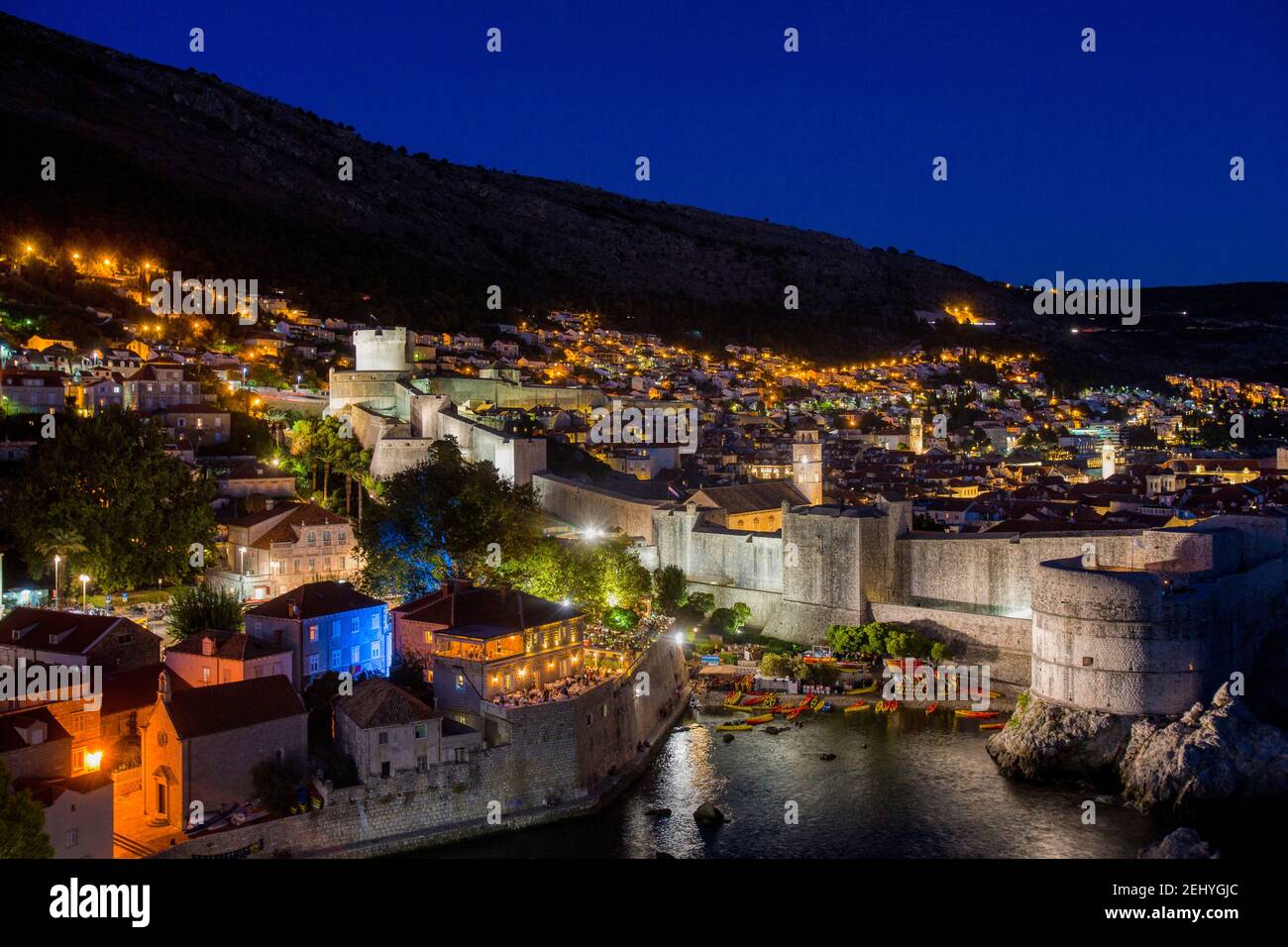 Nachtfotografie einer beleuchteten Stadt Dubrovnik mit Mauer, Berg und dunkelblauem Himmel Stockfoto