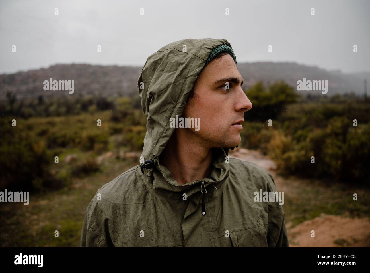 Junger fittlicher männlicher Athlet, der sich auf Schotterberg konzentriert Weg voran mit Büschen und Hügeln hinter ihm Stockfoto