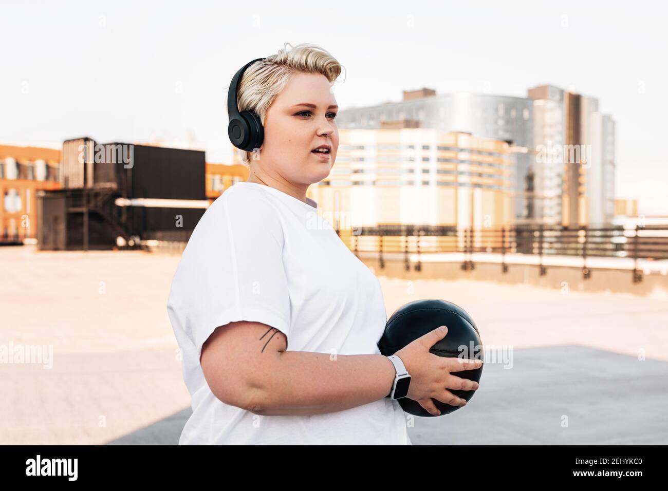 Junge Frau trägt Kopfhörer Training mit einem Medizinball Stockfoto