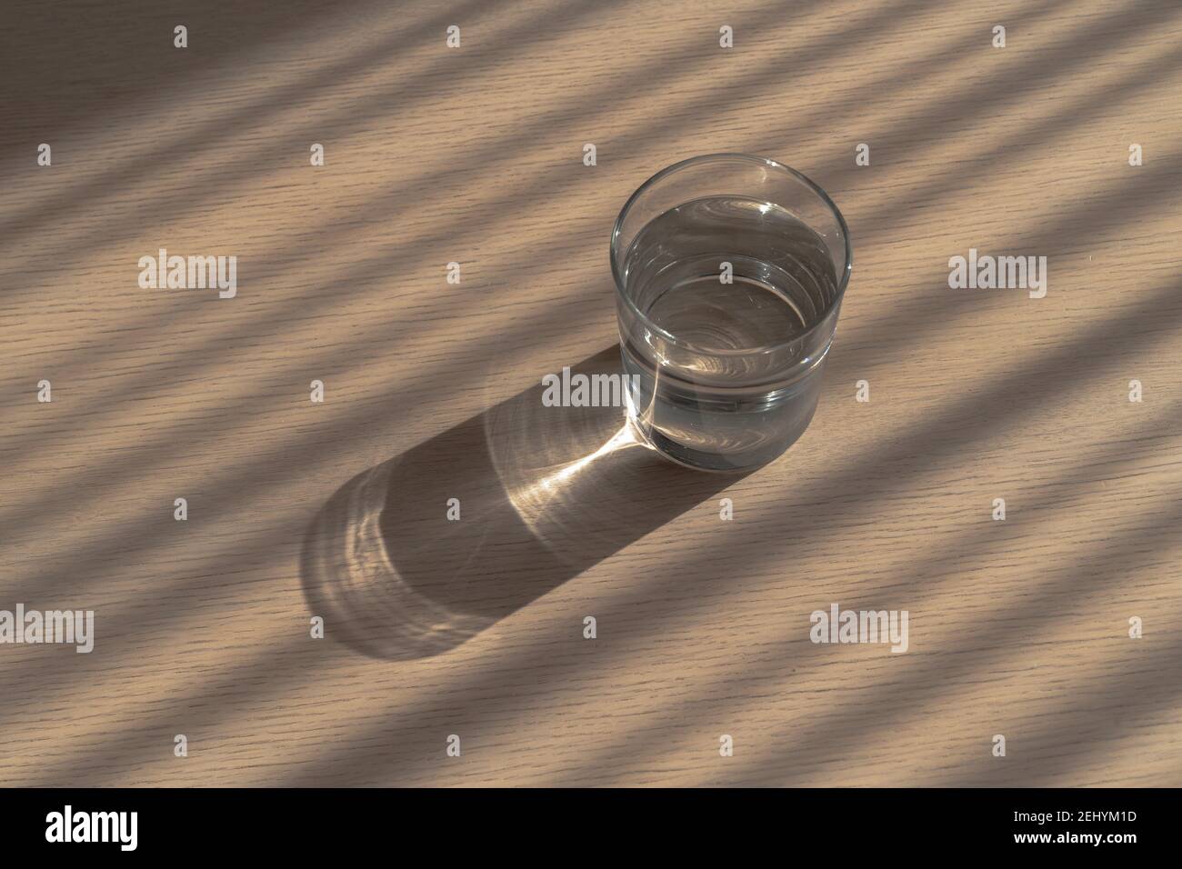 Ein rundes Glas sauberes klares Trinkwasser auf einem Tisch mit wunderbaren Schatten- und Brechungsmustern. Das Problem des Flüssigkeitsverbrauchs. Stockfoto
