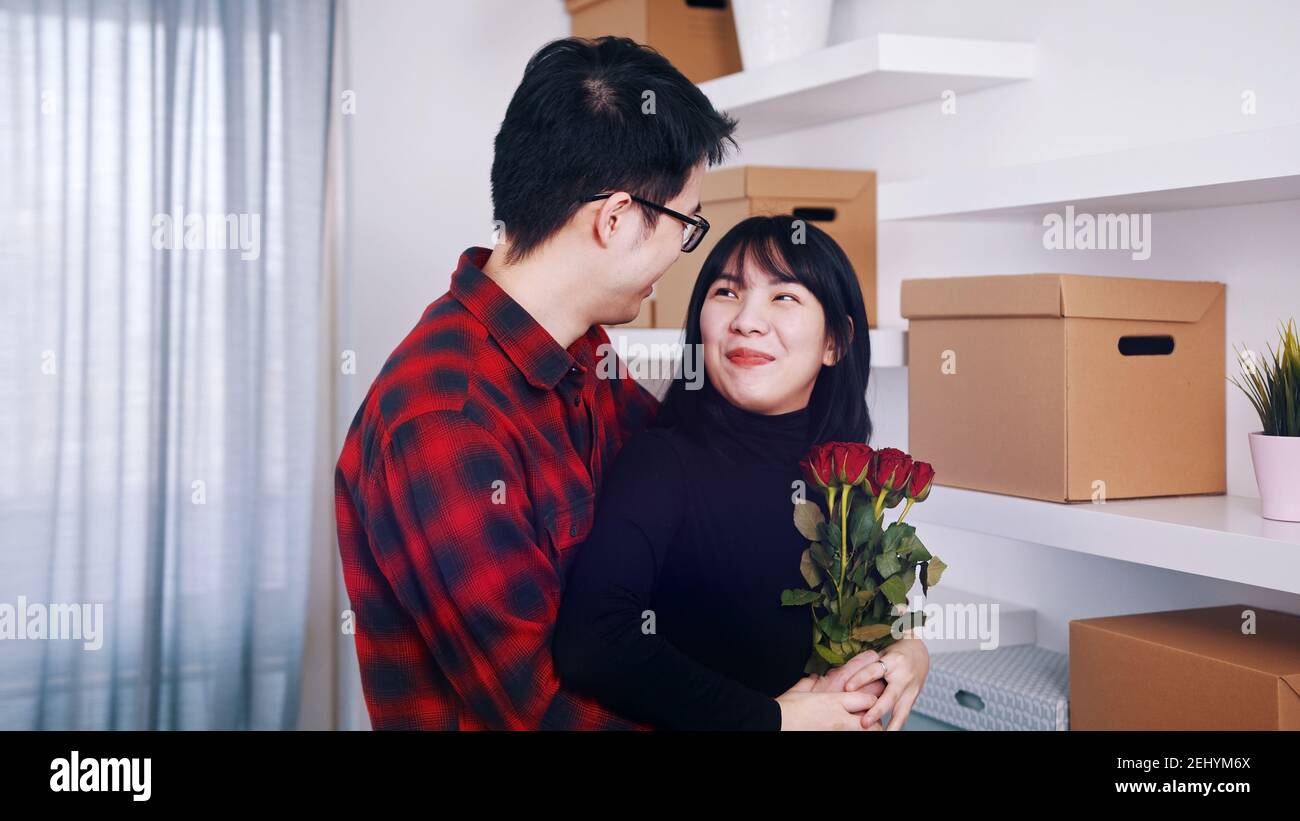Alles Gute zum Jahrestag. Ehemann umarmte seine Frau in der neuen Wohnung. Frau mit roten Rosen. Hochwertige Fotos Stockfoto