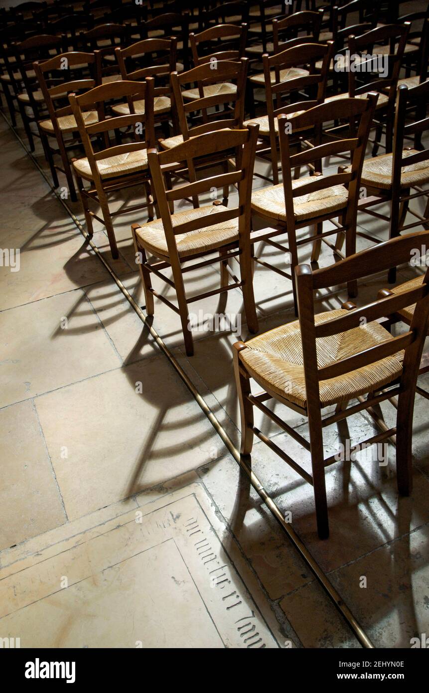 Reihen leerer Holzstühle werfen Schatten in einem schwach beleuchteten Raum in einer Kirche in Frankreich Stockfoto