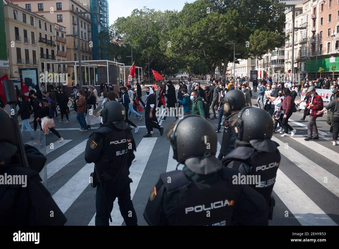 Malaga, Spanien. Februar 2021, 20th. Demonstranten marschieren entlang einer Straße, während Polizeibeamte während der Demonstration Wache stehen. Der Rapper Pablo Hasel wurde wegen der Verherrlichung des Terrorismus und der Beleidigung der spanischen Krone und der staatlichen Institutionen durch seine Lieder und Tweets verurteilt. Nach seiner Inhaftierung in den letzten Tagen sind in mehreren Städten heftige Unruhen ausgebrochen, als Reaktion auf die Meinungsfreiheit. Kredit: SOPA Images Limited/Alamy Live Nachrichten Stockfoto