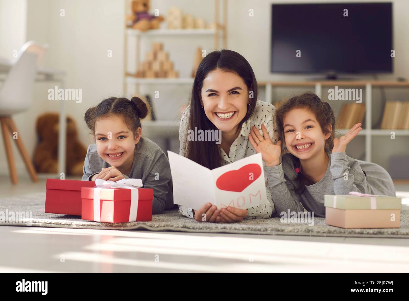 Mutter mit einer Postkarte in den Händen, die auf dem Boden mit ihren Töchtern unter den Geschenken liegt. Stockfoto