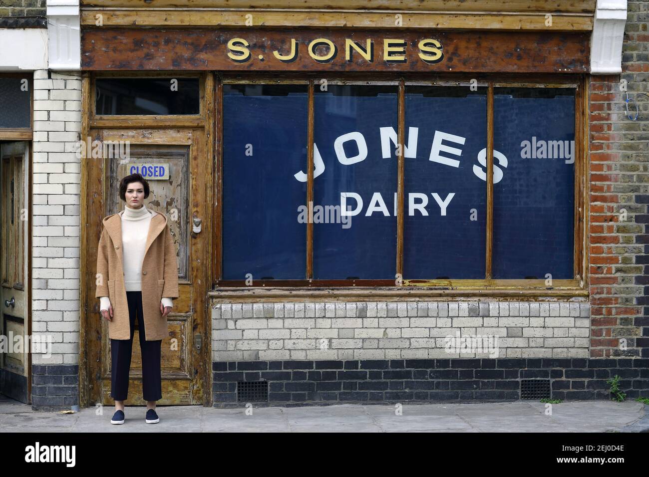Junge Frau, die von der städtischen Ladenfront aus mit einem geschlossenen Schild vor der Tür in London steht. Stockfoto