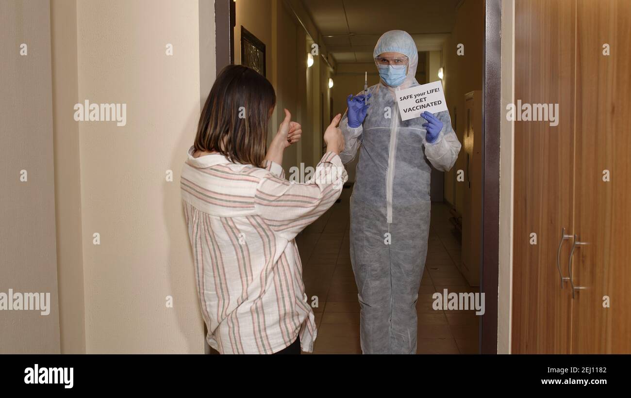 Medizinisches Personal im Anzug mit Aufschrift Text auf Papier Safe your Life Impfen Sie sich bei einer jungen Frau zu Hause und bieten Sie eine Impfung gegen das Coronavirus Covid-19 an. Frau stimmt gerne mit Arzt Stockfoto