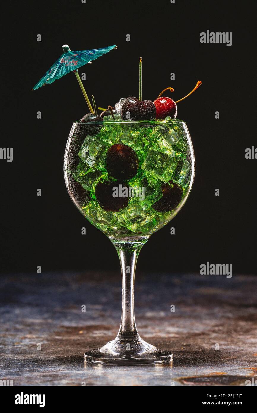 Grüner Cocktail mit Eis und Kirschen in einem Glas dekoriert Mit Sonnenschirmen Stockfoto