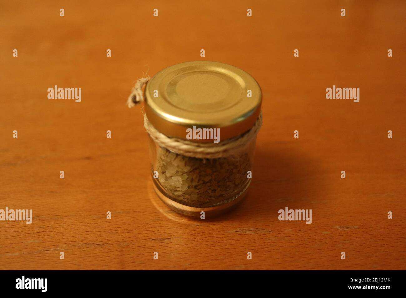 Kleines Glas gefüllt mit Salz und Kräutern mit einem goldenen Deckel auf der Oberseite und ein Band umwickelt es auf einer hölzernen Oberfläche. Stockfoto