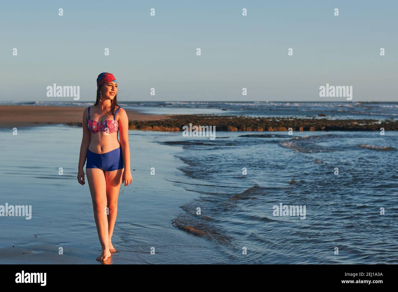 Eine glückliche Frau im Badeanzug, die am Strand entlang geht und schaut Weg Stockfoto