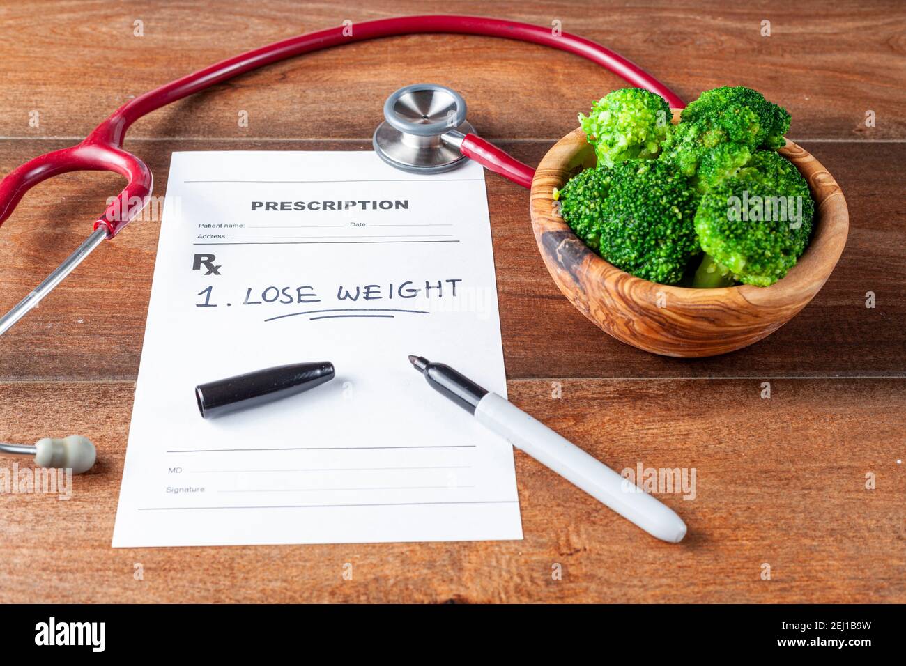 Nahaufnahme schräges Bild eines Arzttisches mit einer Schüssel mit Brokkoli, Stethoskop, Stift und einem Rezept, das einen Artikel 'Gewicht verlieren' verordnet hat Stockfoto