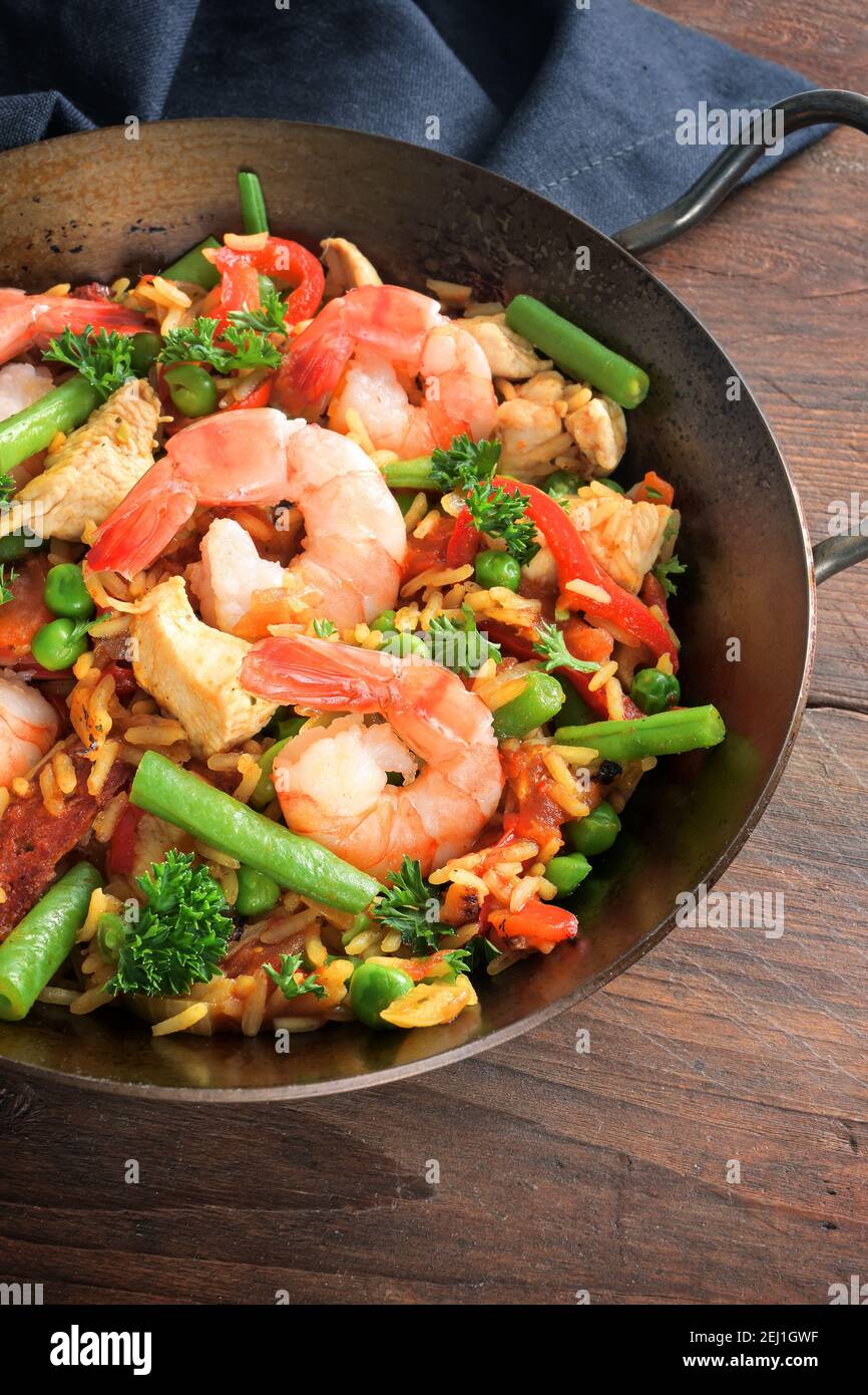 Meeresfrüchte-Gericht mit Reis, Garnelen, Hühnerfleisch und Gemüse in einer kleinen Paella-Pfanne auf einem dunklen rustikalen Holztisch, ausgewählte Fokus, enge Schärfentiefe Stockfoto