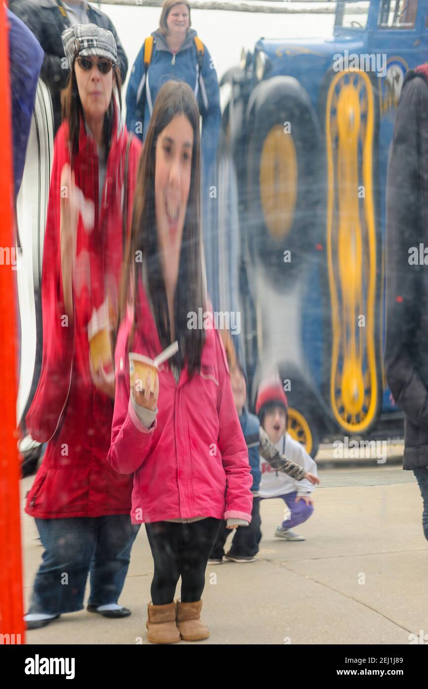 Funhouse Spiegel, das Bild eines jungen Mädchens in einer roten Jacke, spiegelt sich auf der Oberfläche eines verzerrenden Spiegels am Navy Pier, Chicago, Illinois. Stockfoto