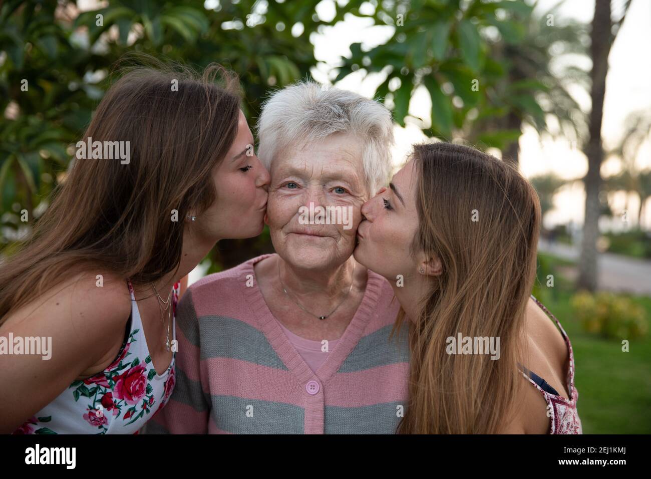 Eine Großmutter bekommt während des National Grosselters Day einen Kuss auf die Wangen von ihren Enkeltöchtern und sie ist sehr glücklich. Stockfoto